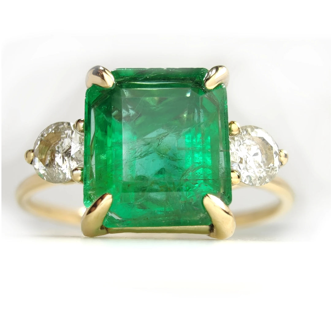 Frontal perspective view of a handcrafted 18K yellow gold three-stone ring with a central emerald and diamond accents