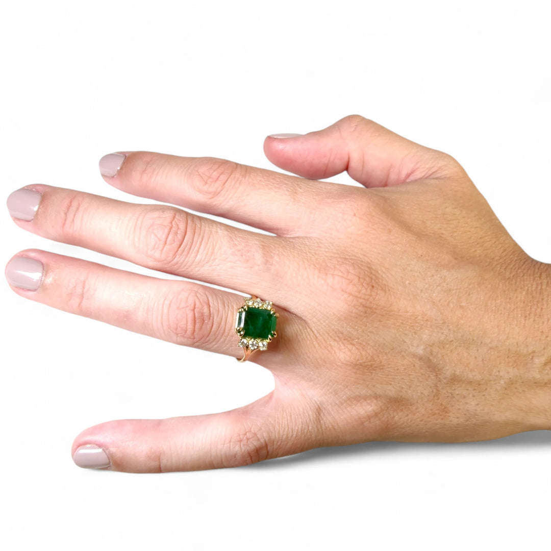 Elegant emerald and diamond engagement ring in 18K yellow gold worn by a female model showcasing the entire hand