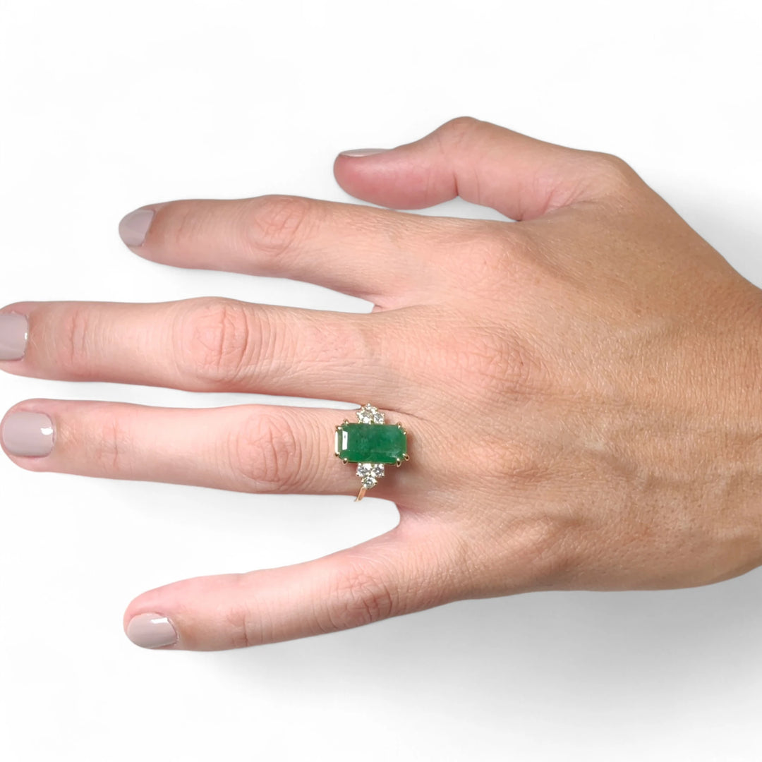 Stunning 18K yellow gold engagement ring with an emerald centerpiece and diamonds worn by a female model on her full hand