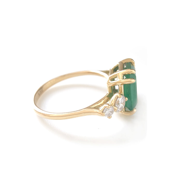 Second left side view of a women’s engagement ring in 18K yellow gold featuring a central emerald cut emerald and round diamonds