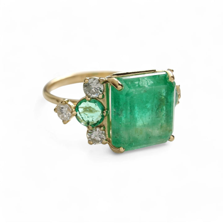 Alternate right side view of a contemporary 18K yellow gold engagement ring with emerald and diamond accents