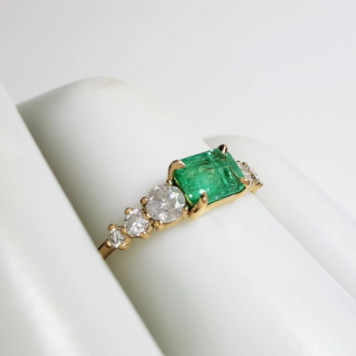 Right side view of a handcrafted 18K yellow gold ring with an emerald centerpiece and diamonds in a tapered design