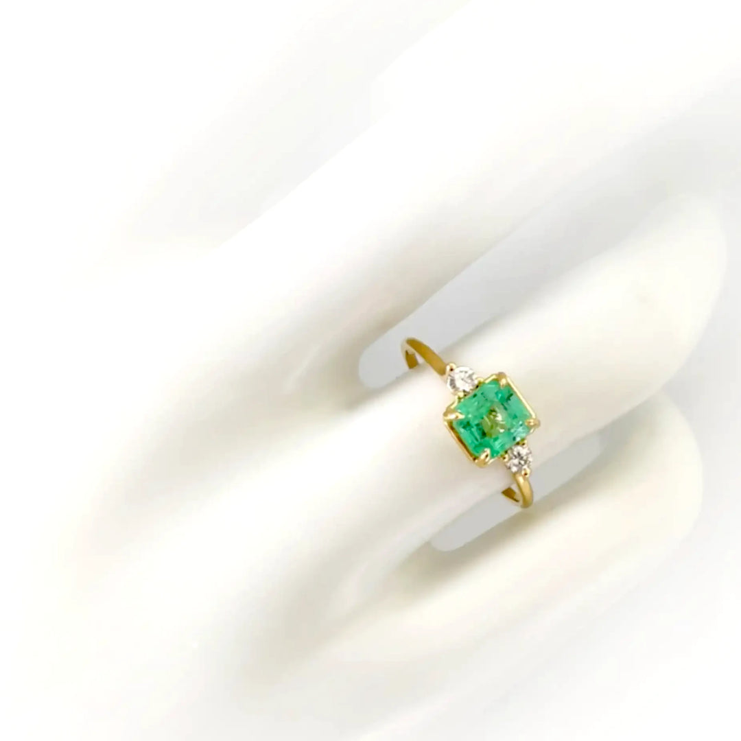 18K gold emerald engagement ring with a three-stone design shown on a mannequin hand. Perfect for engagements, weddings, or a special gift for her