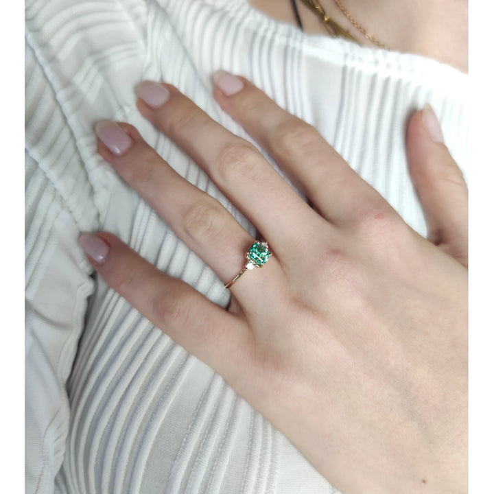 Stunning emerald engagement ring in 18K gold with diamonds, displayed on a model’s hand. A timeless three-stone design ideal for proposals or special gifts