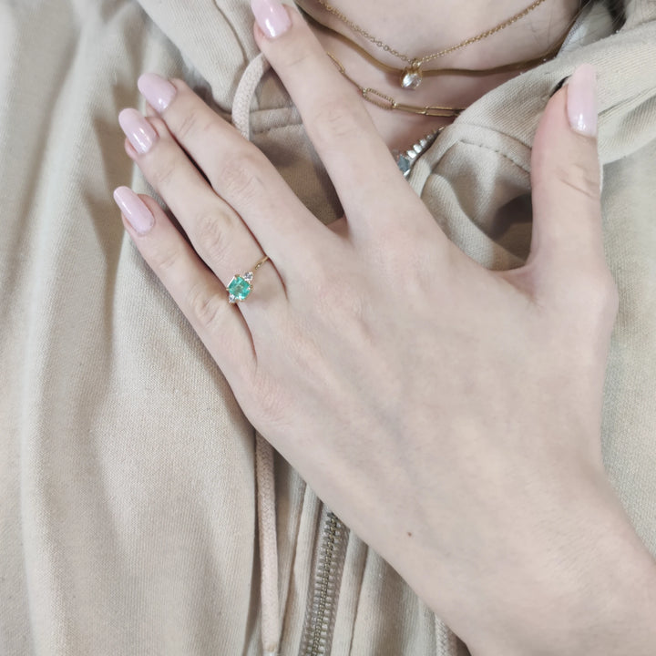 Second pose of a model wearing the 18K gold emerald engagement ring. Features a three-stone design with diamonds, perfect for proposals and gifts