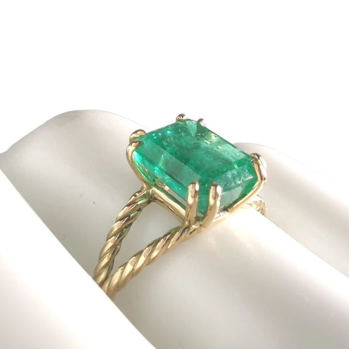 An 18K yellow gold emerald engagement ring displayed on a mannequin’s hand, featuring a central octagonal green emerald, ideal for Christmas or engagements