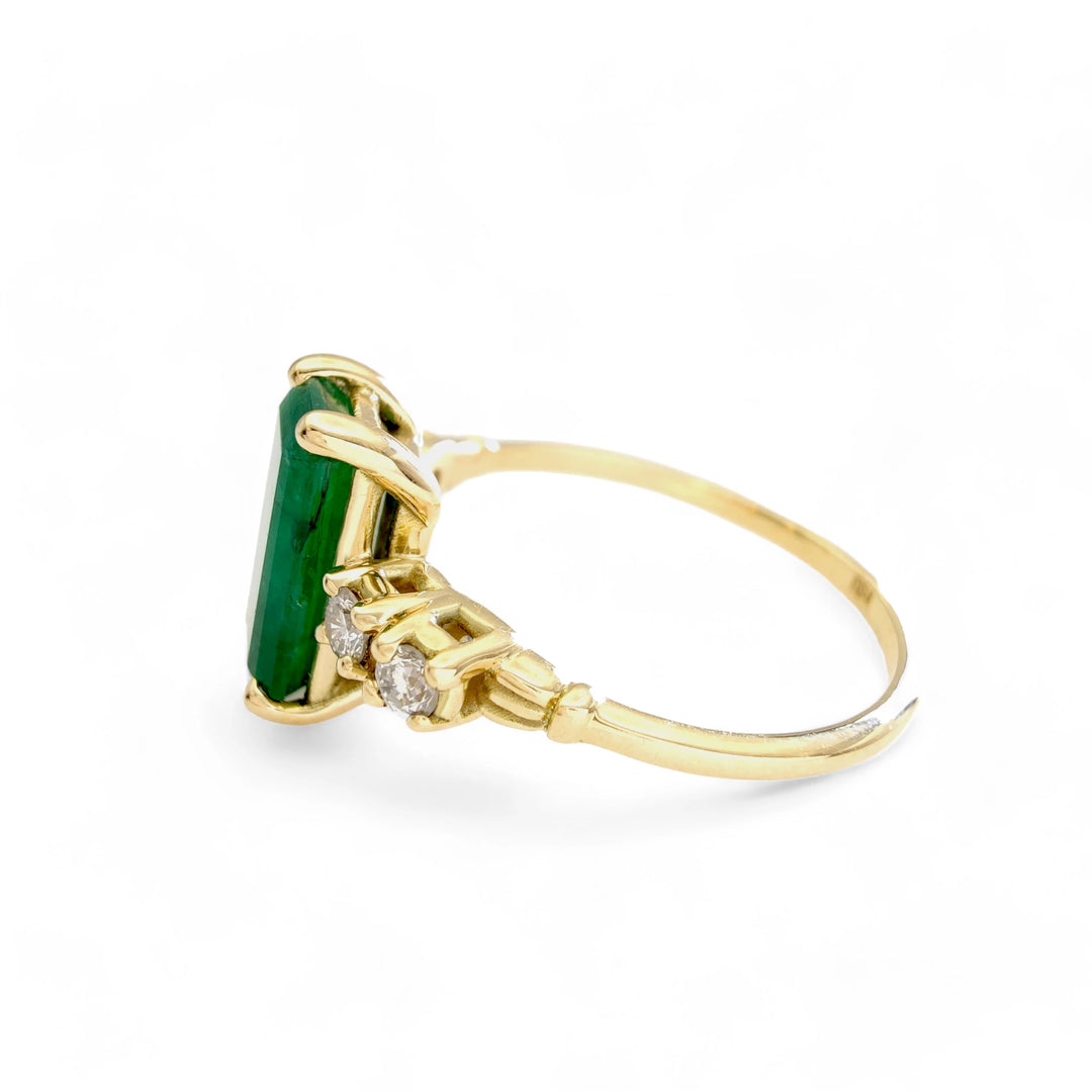 Left horizontal side view of a handcrafted 18K yellow gold engagement ring featuring a central emerald-cut emerald and diamond accents