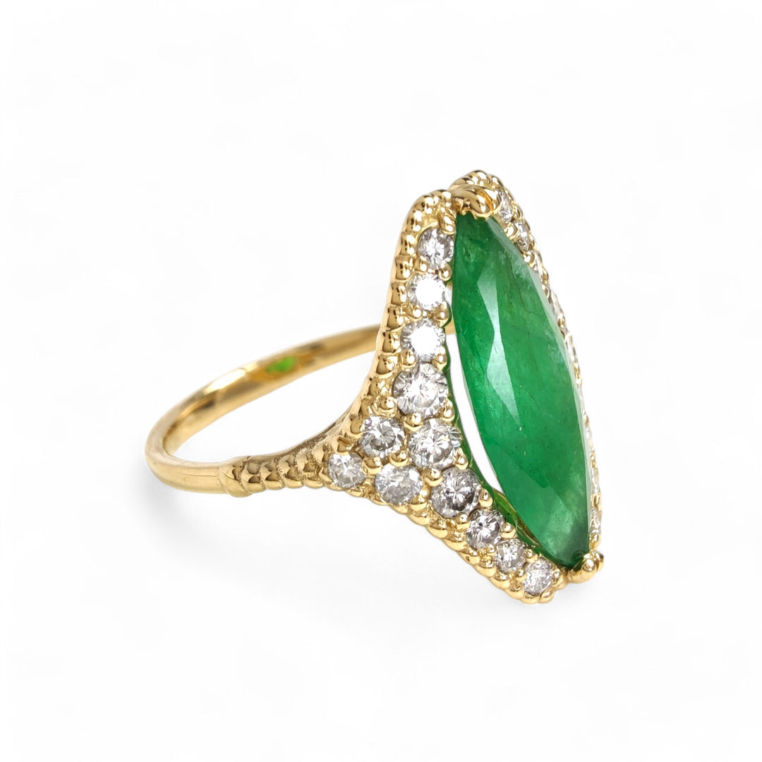 Right side view of a women’s engagement ring in 18K yellow gold with a central marquise emerald and diamond halo, featuring a milgrain band

