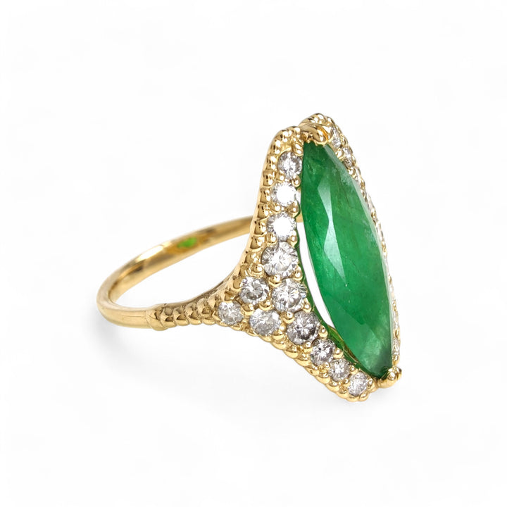 Right side view of a women’s engagement ring in 18K yellow gold with a central marquise emerald and diamond halo, featuring a milgrain band

