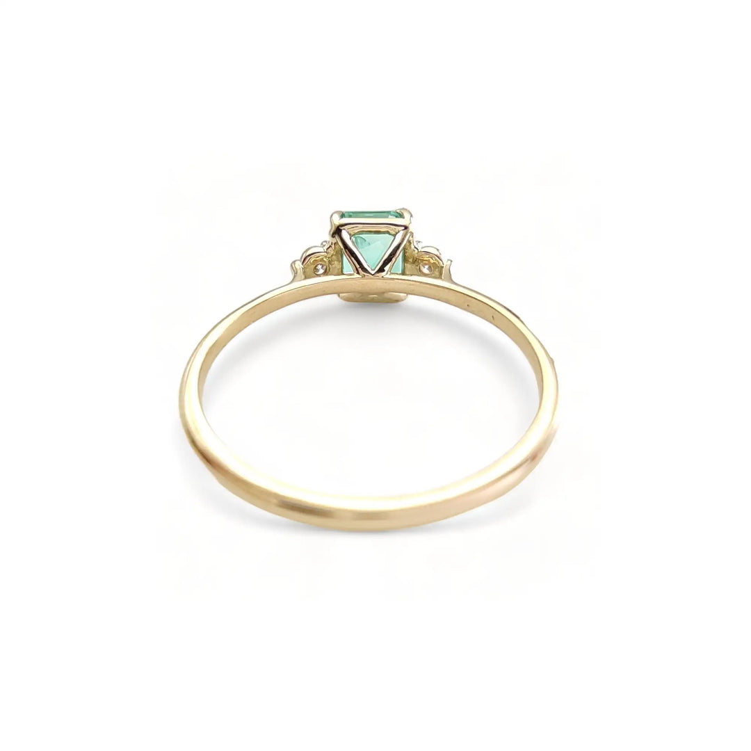 Back view of a women’s 18K yellow gold trilogy engagement ring featuring an emerald centerpiece and diamonds