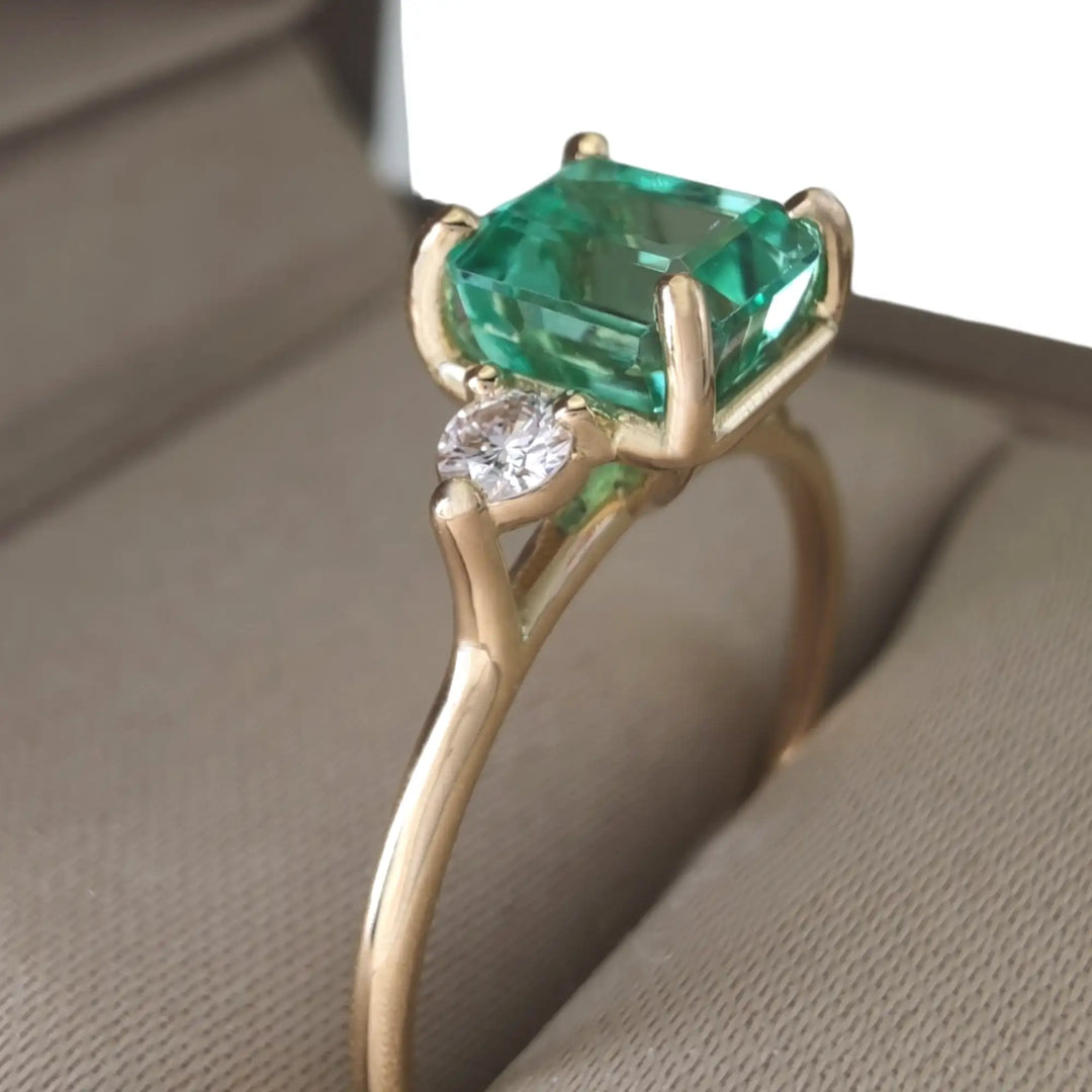 Beautiful 18K yellow gold engagement ring with a central emerald and two diamonds displayed in a jewelry box