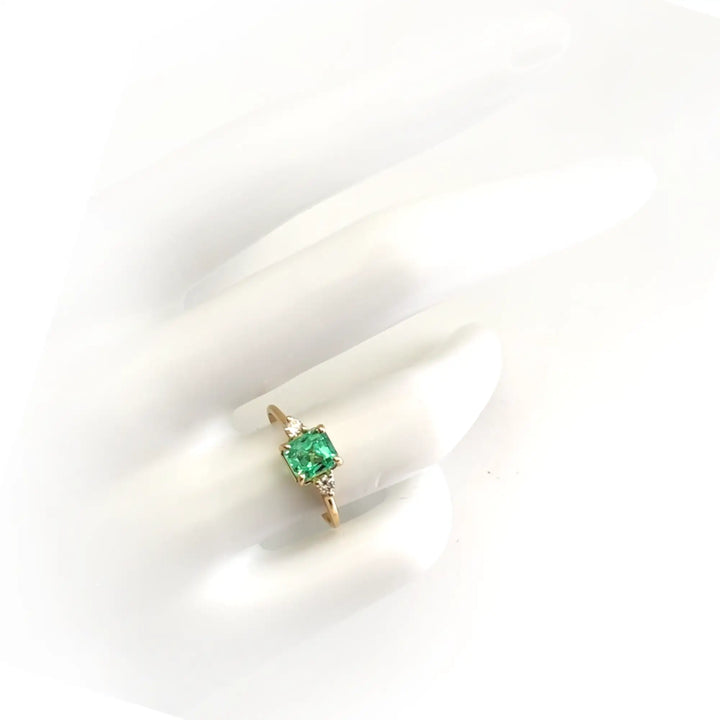 Elegant 18K yellow gold three-stone ring with an octagon-cut emerald and side diamonds displayed on a mannequin hand