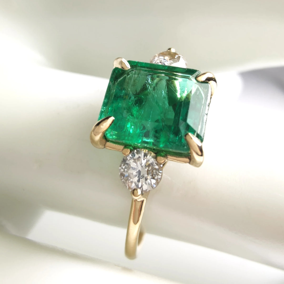 Beautiful 18K yellow gold emerald and diamond three-stone engagement ring worn on a model’s hand