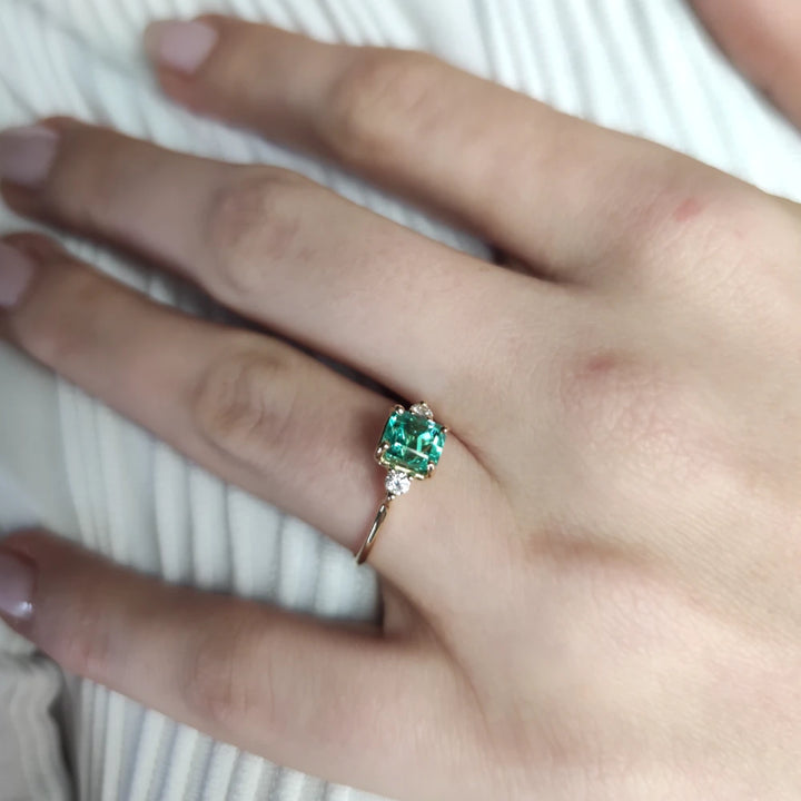 Elegant 18K yellow gold emerald engagement ring worn by a model showcasing its timeless trilogy design