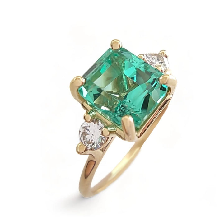 Vertical perspective view of a women’s 18K solid yellow gold engagement ring with a central octagon emerald and two brilliant-cut diamonds