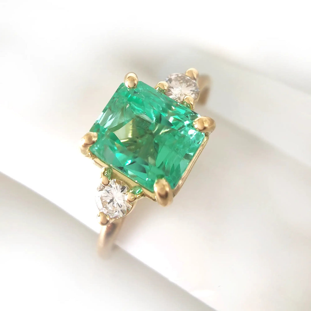 Close-up of a stunning 18K yellow gold three-stone ring with a central emerald and diamond accents on a mannequin finger