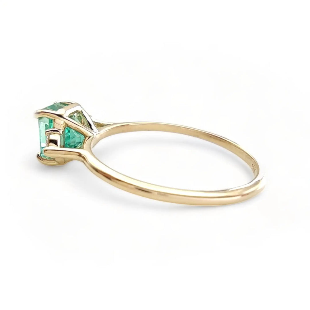 Left side view of a three-stone 18K yellow gold engagement ring with an emerald and diamonds