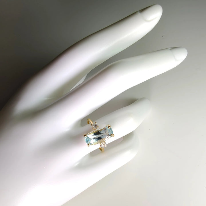 Engagement ring in 18K gold with aquamarine centerpiece and diamonds, displayed on a white mannequin hand