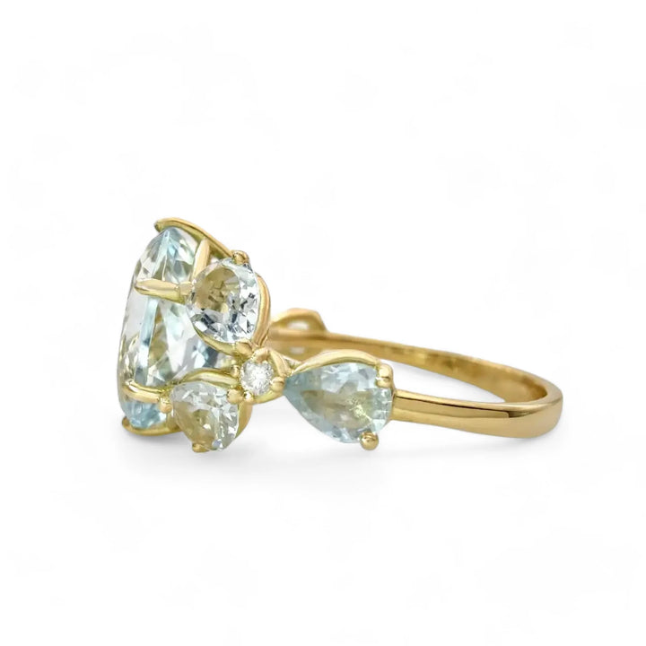 Left side horizontal view of a sculptural women’s ring with an oval aquamarine centerpiece and floral gemstone details