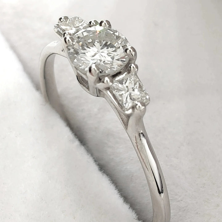A stunning luxury white gold engagement ring featuring a brilliant round-cut diamond as the centerpiece. The elegant design is accentuated by two smaller diamonds on either side, creating a timeless and classic look perfect for proposals or special occasions