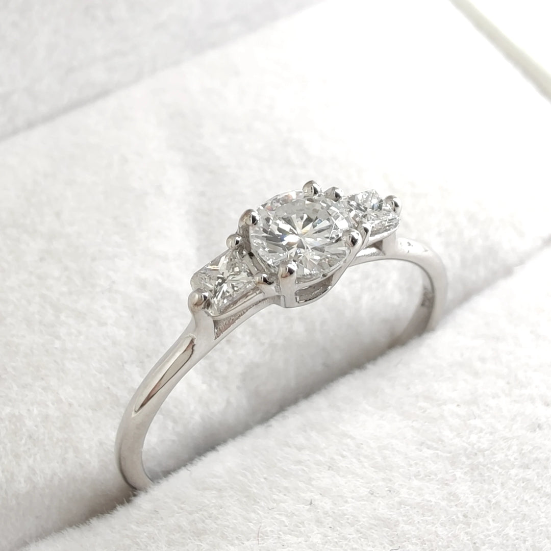 A stunning luxury white gold engagement ring featuring a brilliant round-cut diamond as the centerpiece. The elegant design is accentuated by two smaller diamonds on either side, creating a timeless and classic look perfect for proposals or special occasions