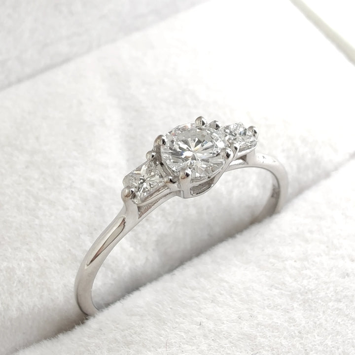 A stunning luxury white gold engagement ring featuring a brilliant round-cut diamond as the centerpiece. The elegant design is accentuated by two smaller diamonds on either side, creating a timeless and classic look perfect for proposals or special occasions