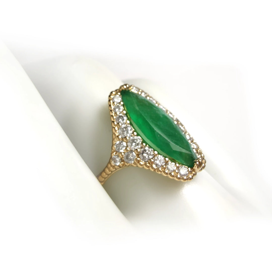 Side view of a unique 18K yellow gold engagement ring with a central marquise emerald, diamond halo, and intricate milgrain detailing displayed on a mannequin