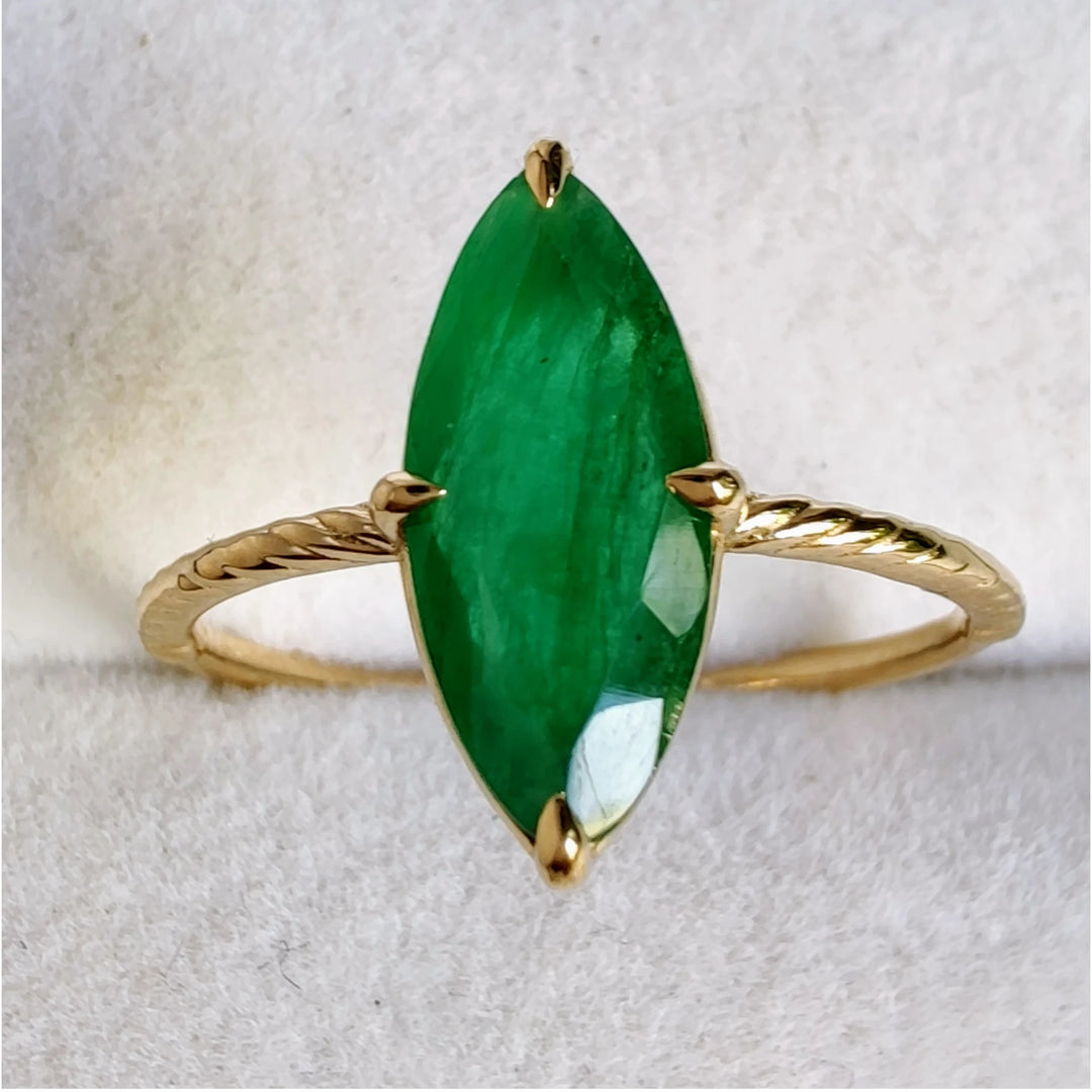 Top view of a vintage-inspired solitaire ring with a marquise-cut emerald set in 18K yellow gold displayed in a jewelry box