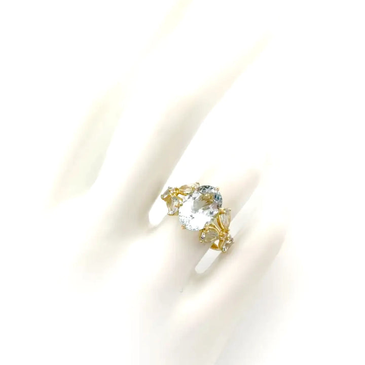 top view of a stunning women’s ring displayed on a white mannequin hand, featuring an oval aquamarine and gemstone floral accents