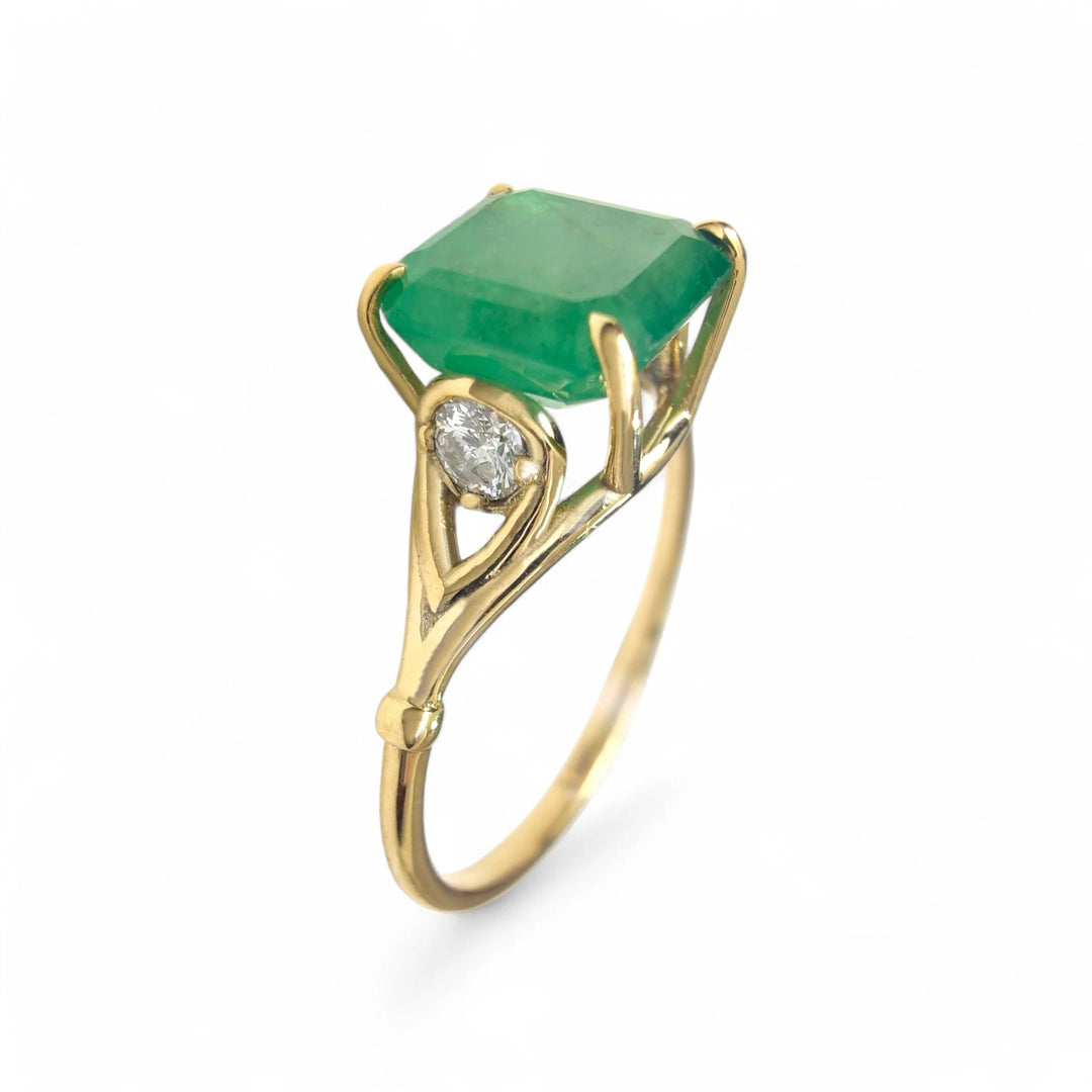 Perspective view of a women’s 18K yellow gold three-stone ring featuring a central octagon emerald and a diamond on each side in a unique contemporary design