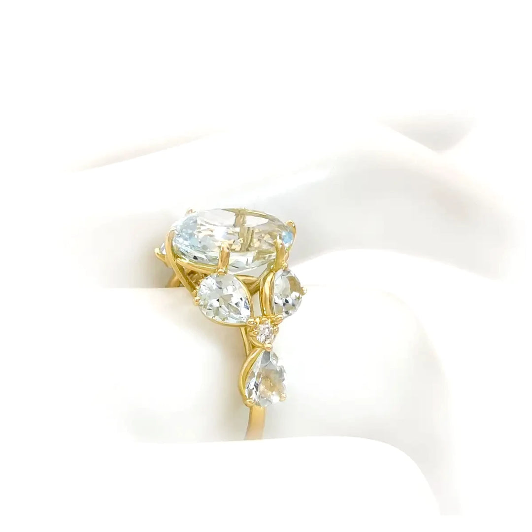 Artistic view of a handcrafted women’s ring with an oval aquamarine, marquise aquamarines, and diamond floral accents displayed on a mannequin hand