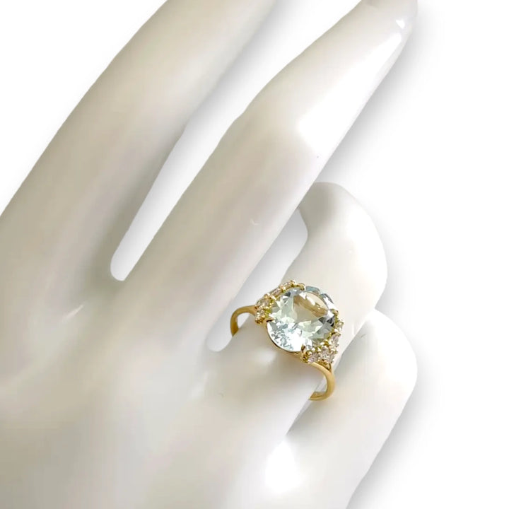 18K yellow gold engagement ring with a natural oval aquamarine and ten brilliant diamonds displayed on a mannequin hand, showcasing exquisite craftsmanship.