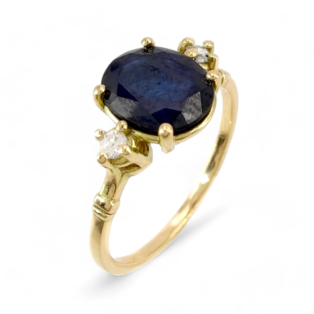 Vertical perspective view of an 18K yellow gold three-stone engagement ring featuring an oval-cut sapphire and a brilliant diamond on each side, perfect for proposals or Christmas gifts