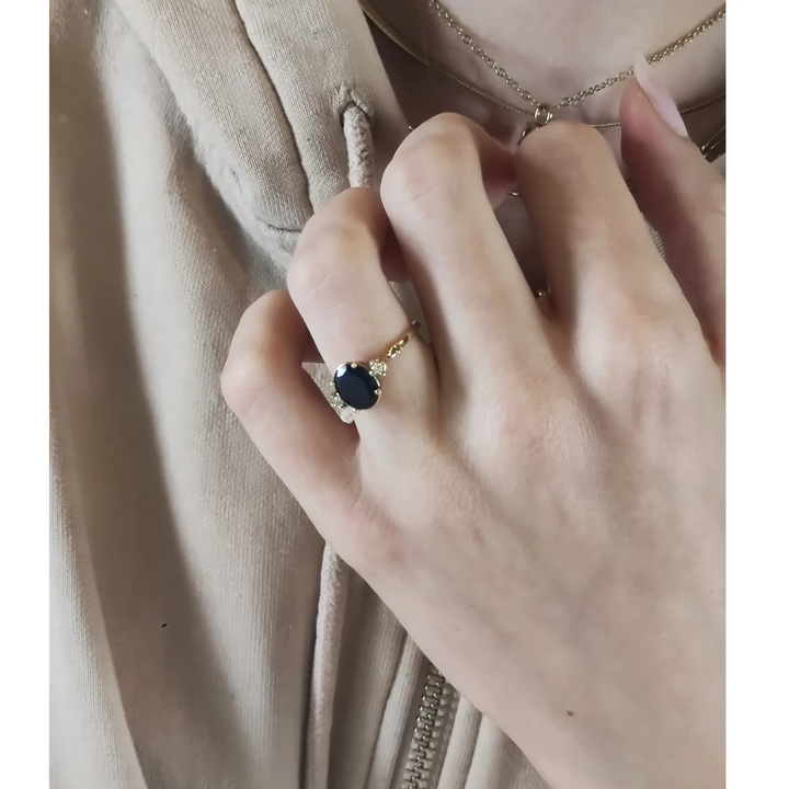 Beautiful three-stone sapphire and diamond ring in 18K yellow gold worn on a model’s hand near her chest in a graceful pose