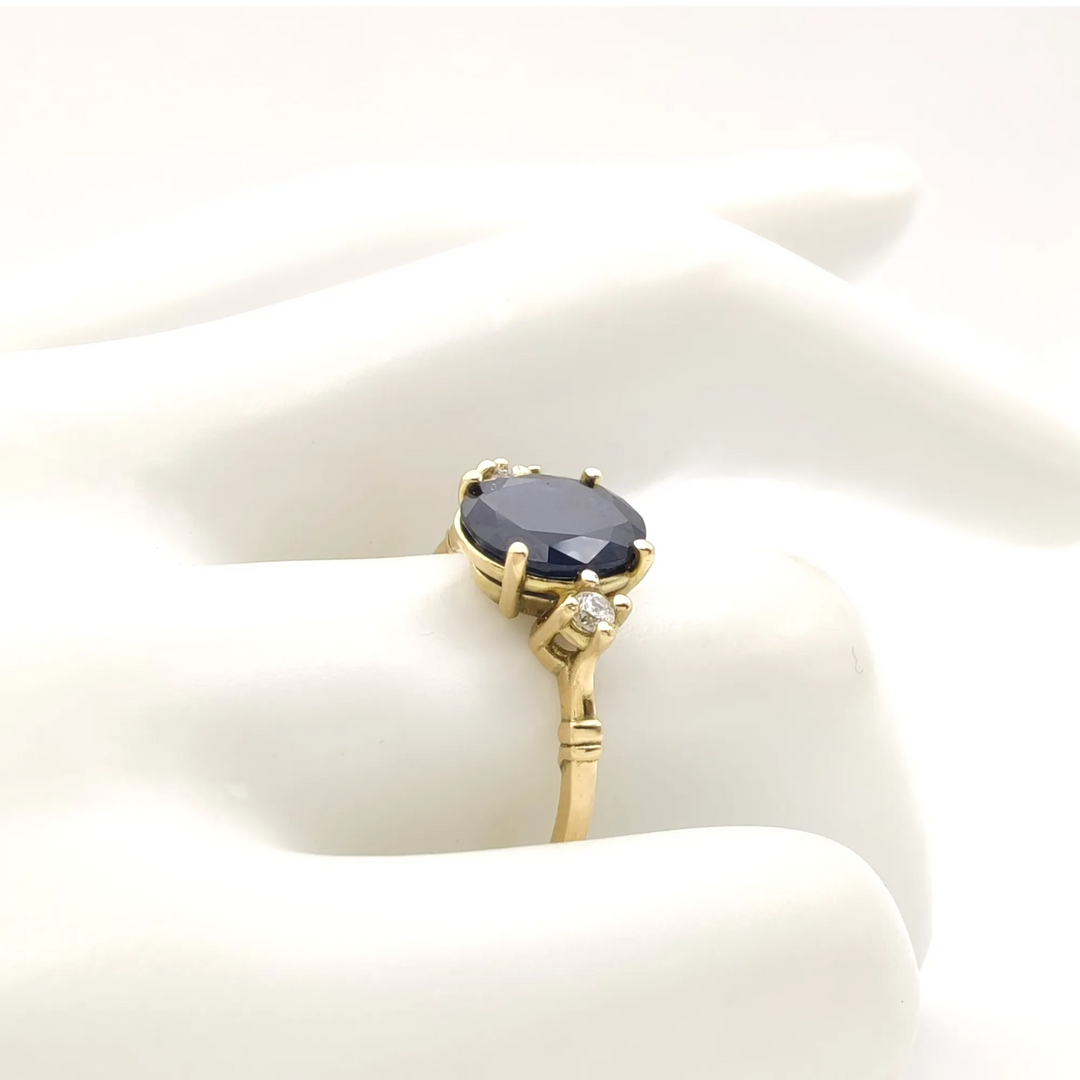 Elegant 18K yellow gold sapphire engagement ring with diamonds, displayed on a mannequin hand in a classic three-stone design