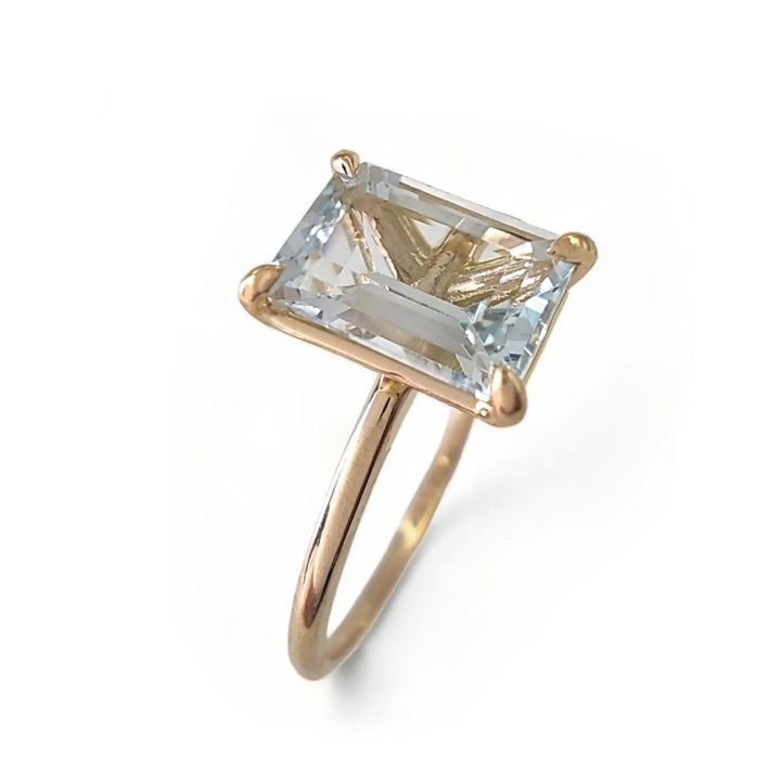 Vertical perspective view of a women’s 18K solid yellow gold solitaire ring with a central aquamarine in a minimalist design