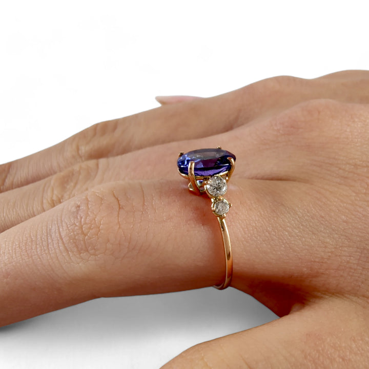 Close-up of a 14K yellow gold Tanzanite engagement ring with diamonds, displayed on a woman’s hand