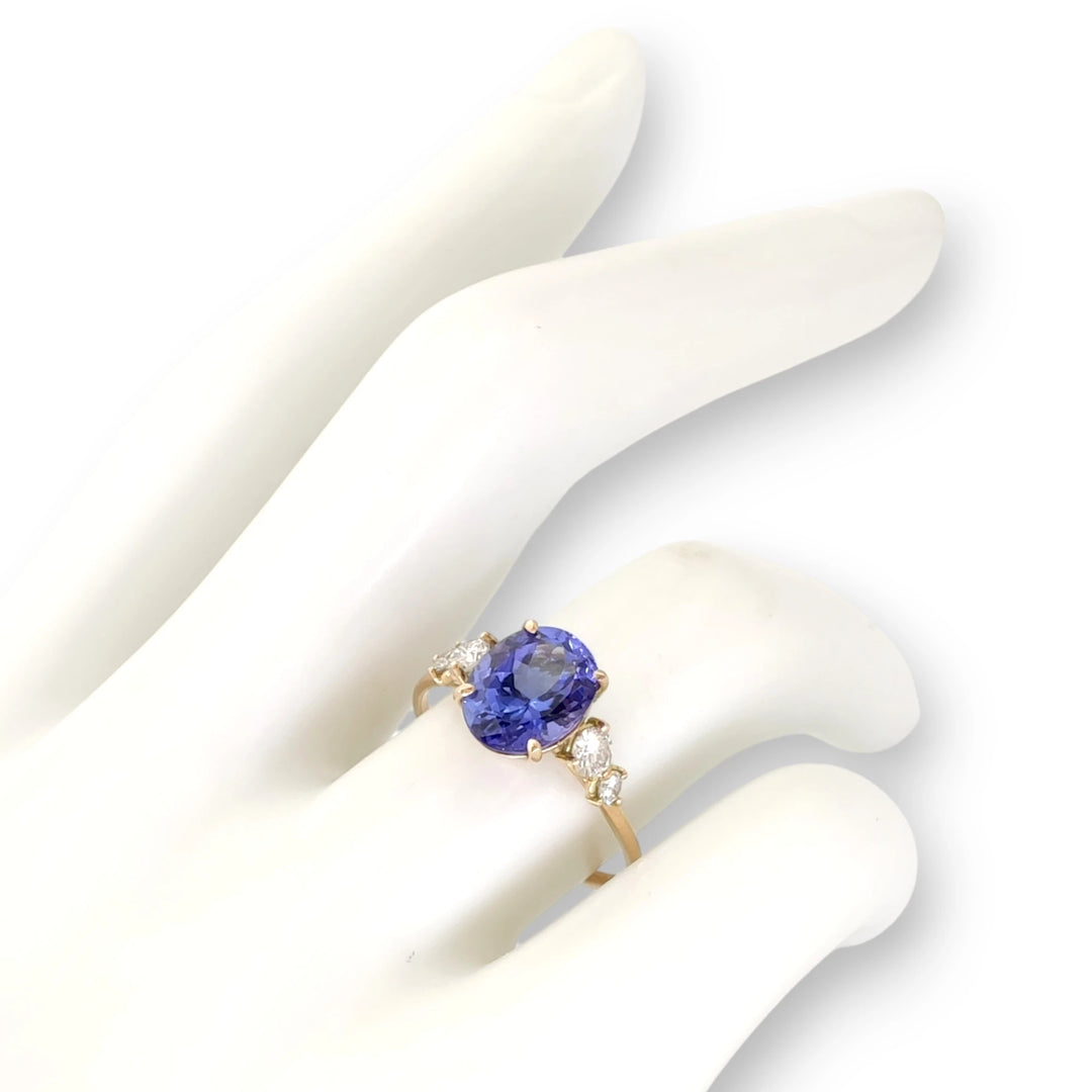 14K yellow gold ring featuring an oval Tanzanite and diamonds, displayed on a mannequin hand