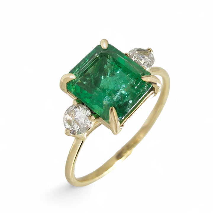 Vertical perspective view of a handcrafted 18K yellow gold three-stone ring with a central emerald cut emerald and round diamond accents