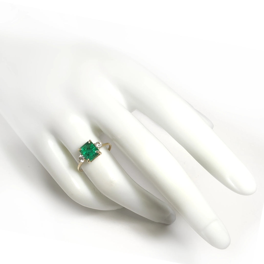 Elegant 18K yellow gold three-stone engagement ring with an emerald and diamonds displayed on a mannequin hand