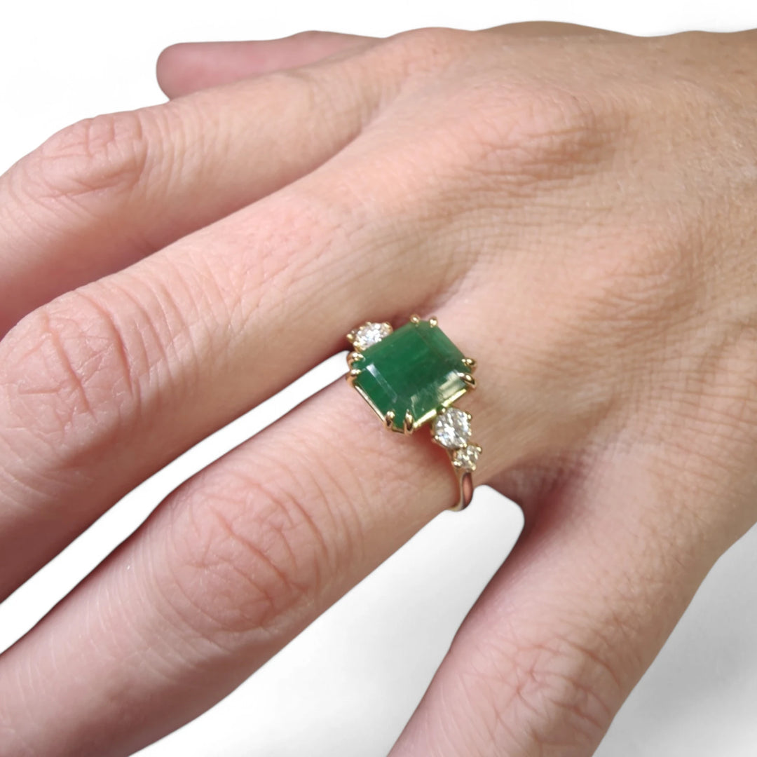 Right side view of a handcrafted 18K yellow gold engagement ring featuring a central emerald and diamond accents in a tapered design