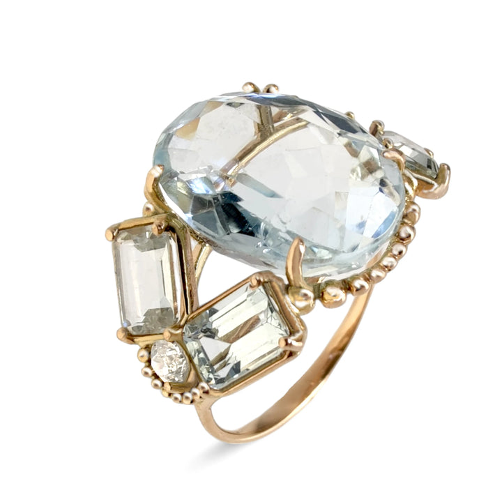 Vertical perspective view of a bold vintage-style women’s ring in 14K yellow gold featuring an oval aquamarine centerpiece, emerald-cut aquamarines, and brilliant diamonds